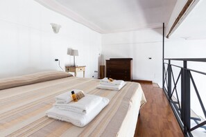 A hotel room with a large bed, a wooden dresser, a nightstand with a lamp, and a balcony with a metal railing.