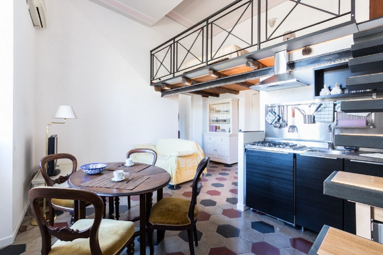 A dining area with a round table, chairs, and a kitchen with a stove and cabinets.