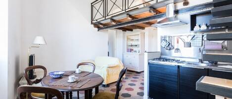 A dining area with a round table, chairs, and a kitchen with a stove and cabinets.