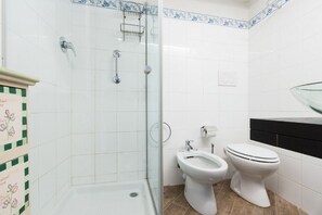 A bathroom with a shower, bidet, toilet, and a glass shower enclosure.