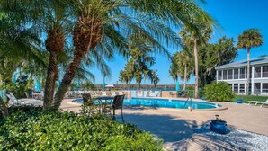 A pool area with lounge chairs and umbrellas, surrounded by palm trees and greenery.
