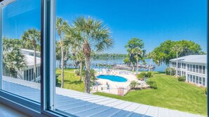 A view of a backyard with a swimming pool, palm trees, and a dock extending into a lake.