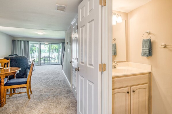 A hotel room with a dining area, a large sliding glass door to a balcony, and a bathroom with a sink and mirror. - River Bend B212 (Welaka)