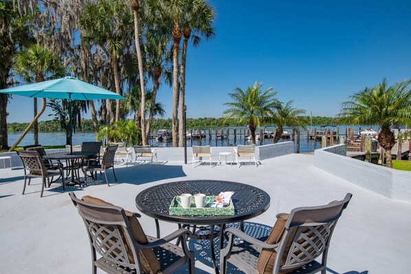 Un patio exterior con una mesa redonda y sillas, con vista a una masa de agua con muelles y barcos.