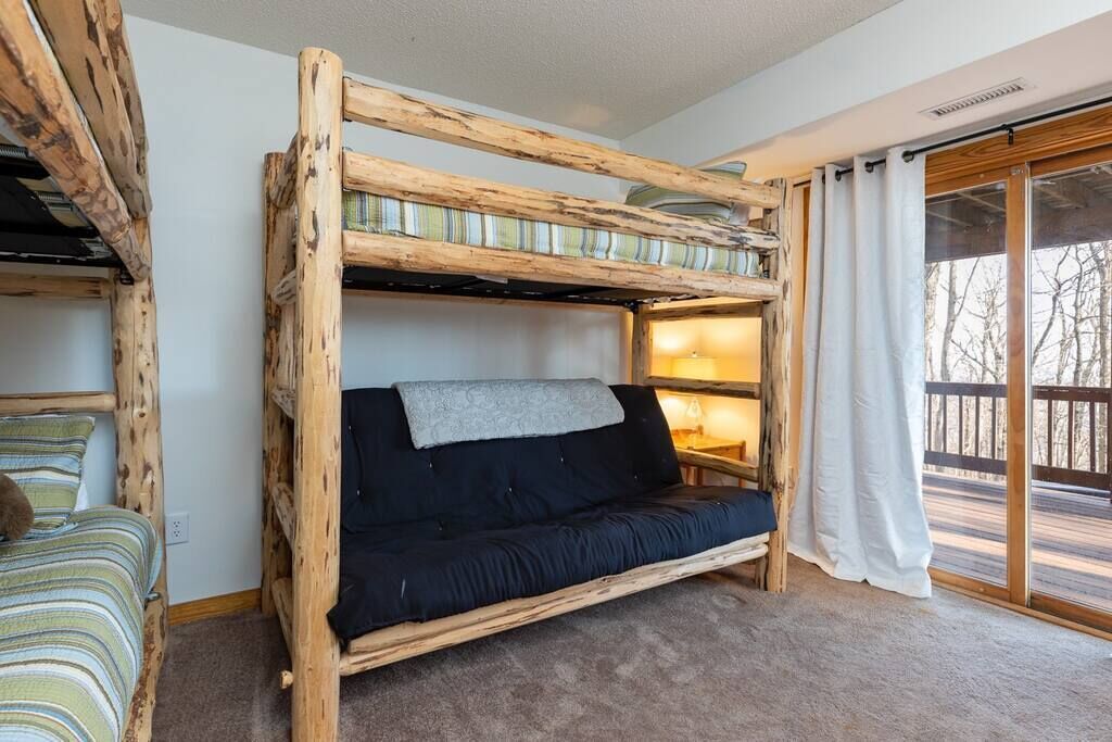 Ein Etagenbett mit dunkler Matratze und Decke, ein Holzkopfstück und ein Fenster mit Vorhängen.
