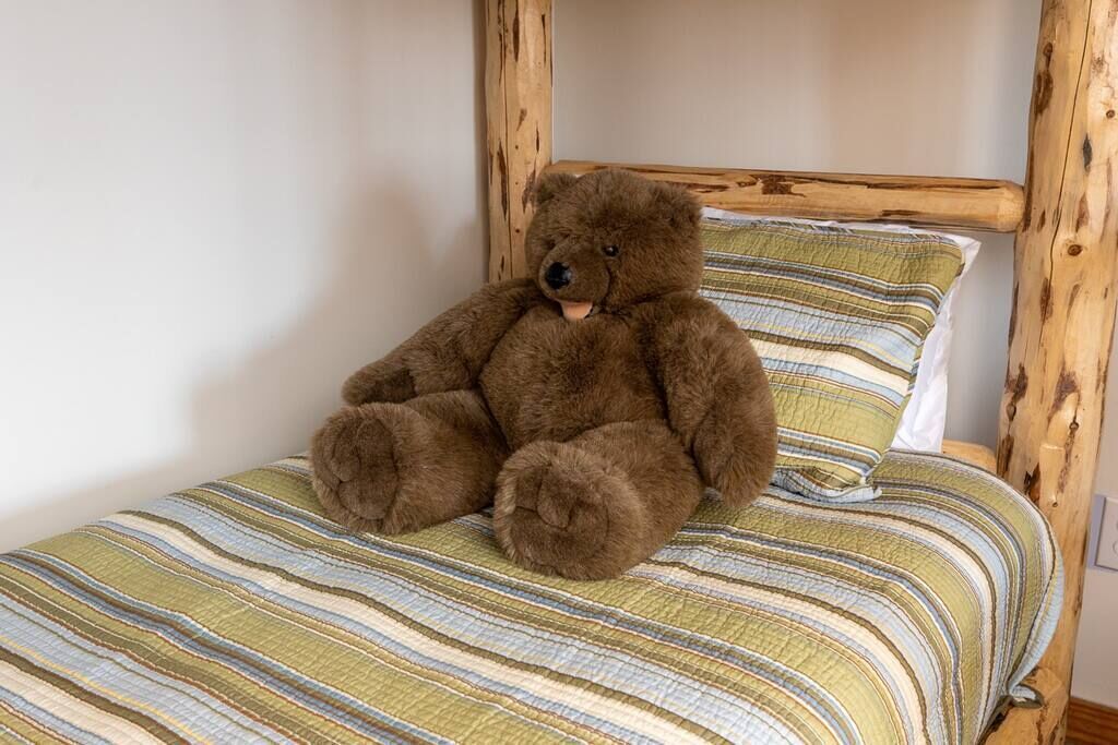A brown teddy bear sitting on a bed with a striped bedspread.