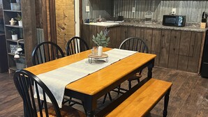 A rustic dining area with a wooden table and benches, surrounded by wooden cabinets and a kitchen area with a microwave. - The Texas Rig - Cabin on Caddo Lake (Karnack)