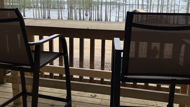 A wooden deck with two chairs facing a body of water and trees. - The Texas Rig - Cabin on Caddo Lake (Karnack)