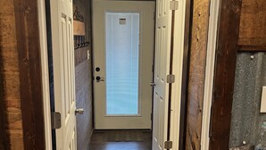 A narrow hallway with wooden walls and floors, a door with a window, and a light fixture on the ceiling. - The Texas Rig - Cabin on Caddo Lake (Karnack)