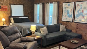 A cozy room with a bed, a sofa, a recliner, a coffee table, and a rug. - The Texas Rig - Cabin on Caddo Lake (Karnack)