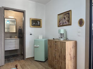 A compact room with a wooden cabinet, a small refrigerator, a coffee maker, and a mirror with a towel hanging on it. - Ecological Studio Flat in Kalyvia Thorikou, Greece (Lagonisi)