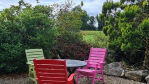 A patio with a round table and two chairs, surrounded by dense greenery and a stone wall. - 1 Bed retreat-Sleeps 2-Secure parking-Garden (Ennis)