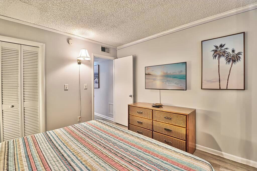 A bedroom with a bed, a dresser, a lamp, and a painting on the wall.