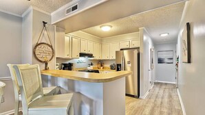 A modern kitchen with white cabinets, a central island, and a dining area with a chair. - Beach & Nightlife 3BR/2.5 BA service dog friendly (North Myrtle Beach)