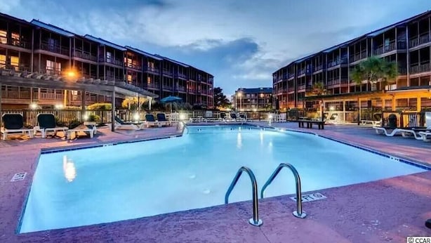A swimming pool with lounge chairs and a building with balconies in the background. - Beach & Nightlife 3BR/2.5 BA service dog friendly (North Myrtle Beach)