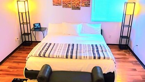 A bedroom with a bed, bedside lamps, a nightstand, a window with blinds, and a floral rug. - Cheerful 3 bedroom house with a beautiful backyard (Tucson)