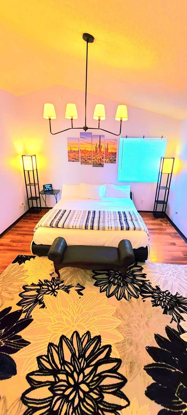 Quarto com cama, abajures, mesa de cabeceira, janela com persianas e tapete floral.