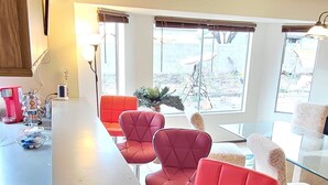 A modern kitchen with a bar area, red bar stools, and large windows offering a view of the backyard. - Cheerful 3 bedroom house with a beautiful backyard (Tucson)