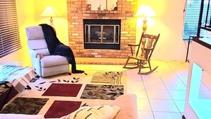 A living room with a brick fireplace, a ceiling fan, and a television mounted on the wall. - Cheerful 3 bedroom house with a beautiful backyard (Tucson)