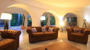 A spacious living area with three brown sofas, a wooden coffee table, and a floor lamp.