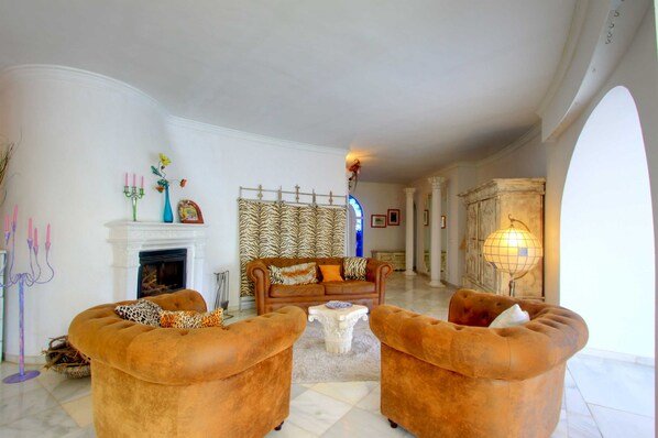 A spacious living room with a fireplace, a patterned sofa, and a chandelier. - 2042 Elegant Villa with Garden, heated Pool and Spacious Layout (Marbella)