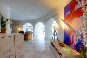 Un hall d’entrée spacieux avec un sol en marbre, un canapé, un bureau avec un ordinateur portable et un grand tableau abstrait.