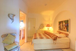 Ein Schlafzimmer mit einem Bett, einem Sessel, einem Spiegel und einem Gemälde an der Wand.