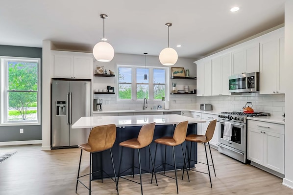 Une cuisine moderne dotée d’un îlot central, d’appareils électroménagers en acier inoxydable et de luminaires suspendus.