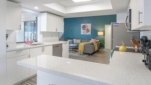 A modern kitchen with white cabinetry, a central island, and a dining area with a sofa and table.