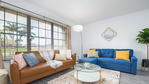 A living room with a brown sofa, a blue sofa, a glass coffee table, and a patterned rug.