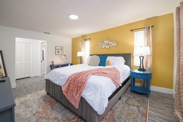 A bedroom with a bed, two nightstands, a wall clock, and a door. - Heated Pool | Game Room | 9 beds | 2 Living Rooms for Groups & Families! PETS OK! (Cape Coral)