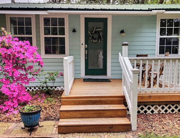 A house with a green door, a porch with wooden steps, and a potted plant with pink flowers. - Tucked away quiet cottage~5 blocks to riverfront and Cumberland Island ferry (St. Marys)