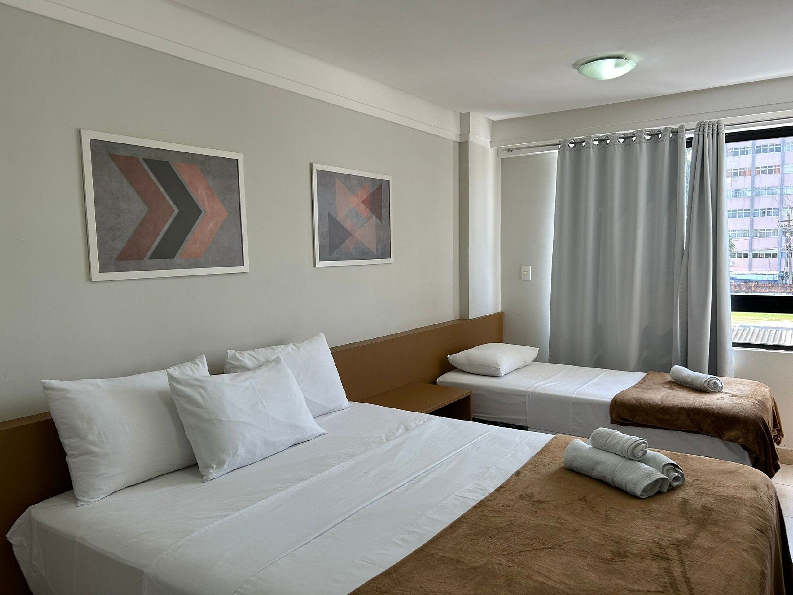 Ein Hotelzimmer mit zwei Betten, einem Fenster mit Vorhängen und zwei abstrakten Bildern an der Wand.