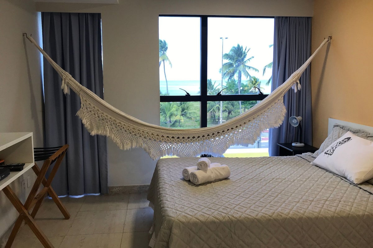 A bedroom with a bed, a hammock, a desk, and a view of the outdoors.