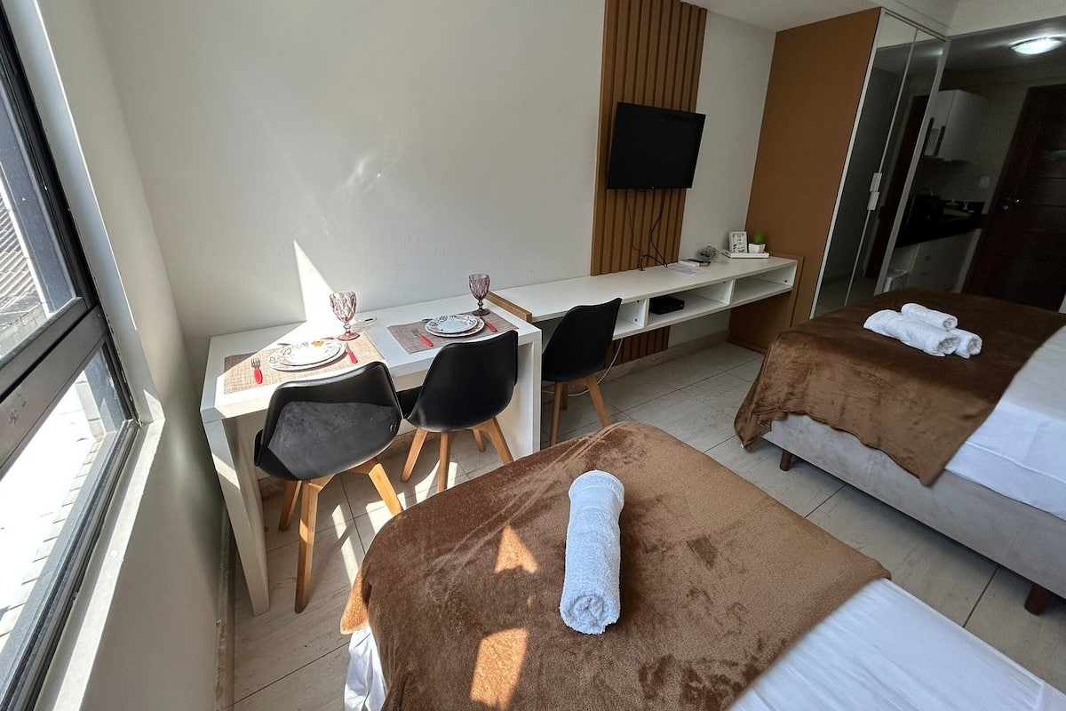 A hotel room with a bed, a desk with chairs, a TV, and a window.