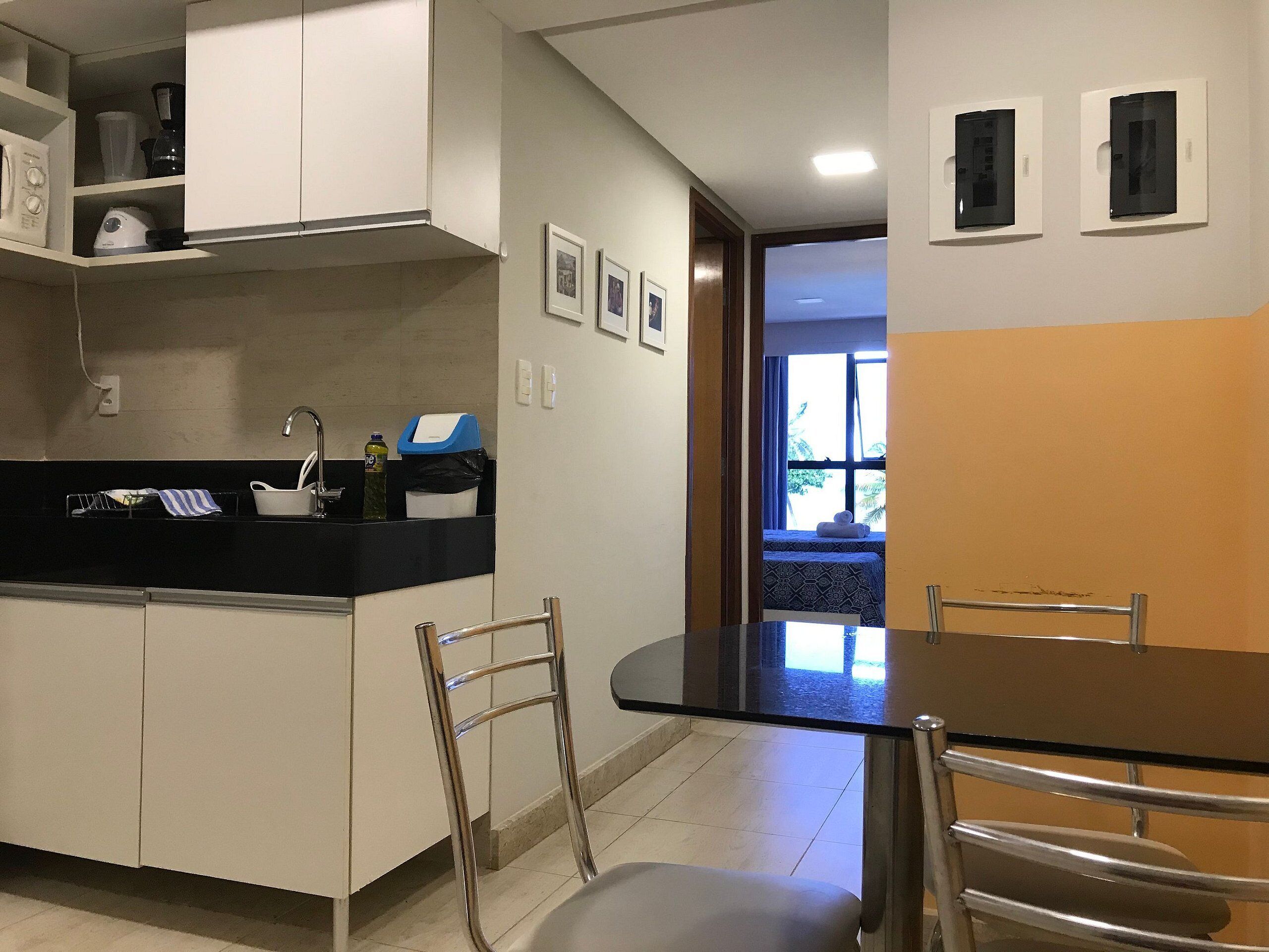 Une cuisine avec des meubles blancs, un plan de travail noir et un coin repas comprenant une table et des chaises.
