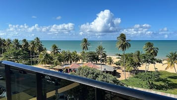 Vista a la playa con palmeras, cielo despejado y océano al fondo.