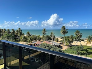 Vista da praia com palmeiras, céu claro e oceano ao longe.