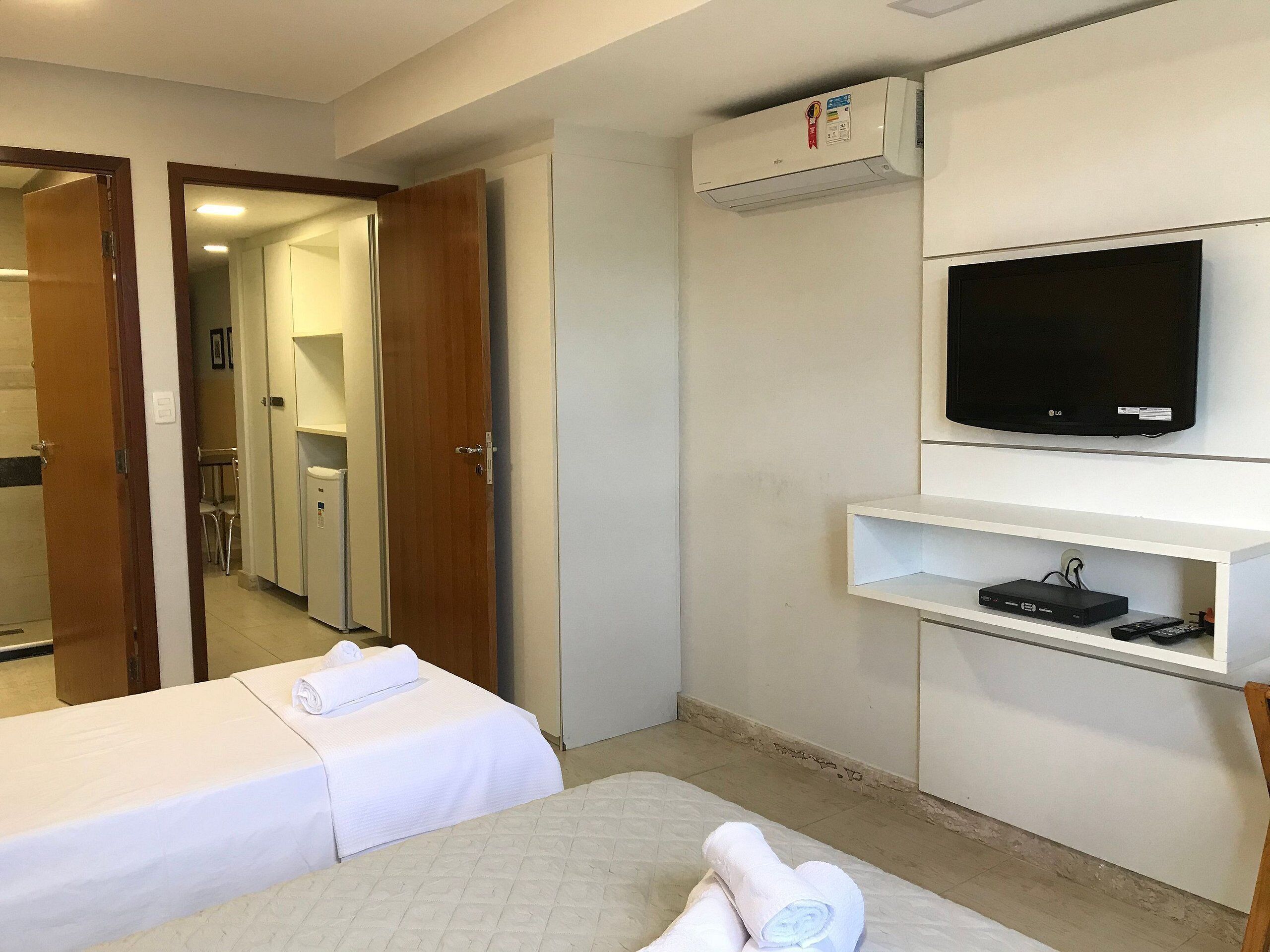 Ein Hotelzimmer mit Bett, Fernseher, einer kleinen Ablage für elektronische Geräte und einer Klimaanlage.