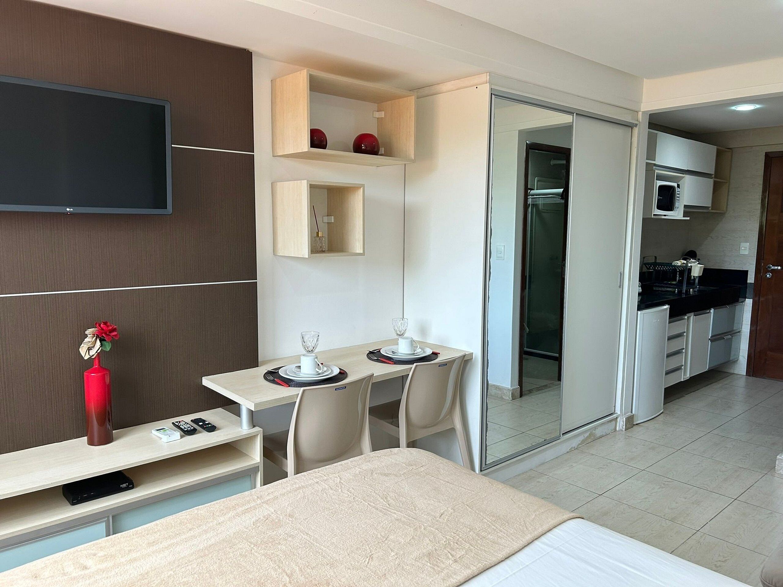 Una moderna camera d'albergo con un letto, una scrivania con un computer, una TV, un'area pranzo con sedie, una cucina con forno a microonde e una porta scorrevole per la zona doccia.