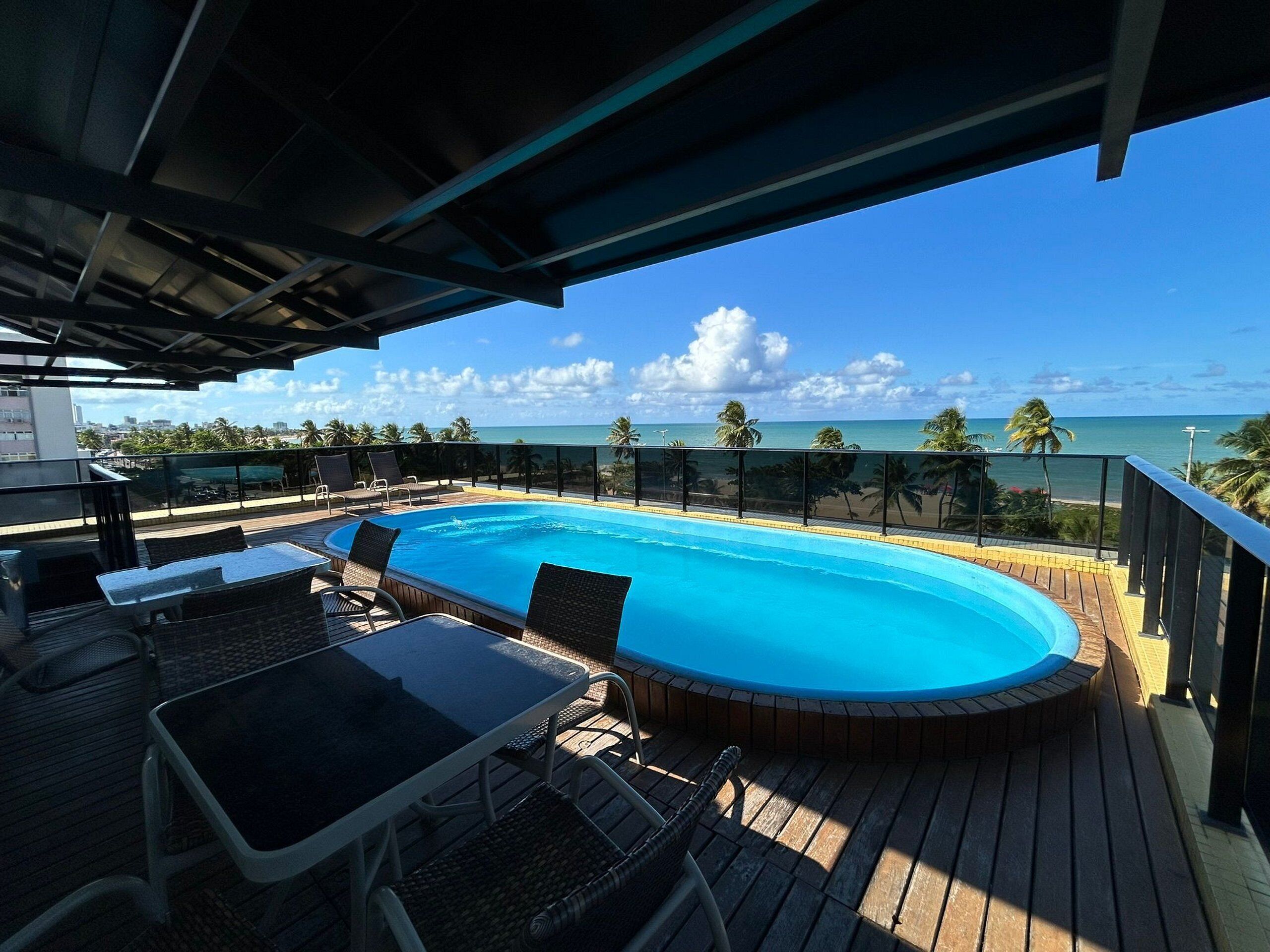 Piscina en la azotea con vista al océano, rodeada de sillas de descanso y una mesa.