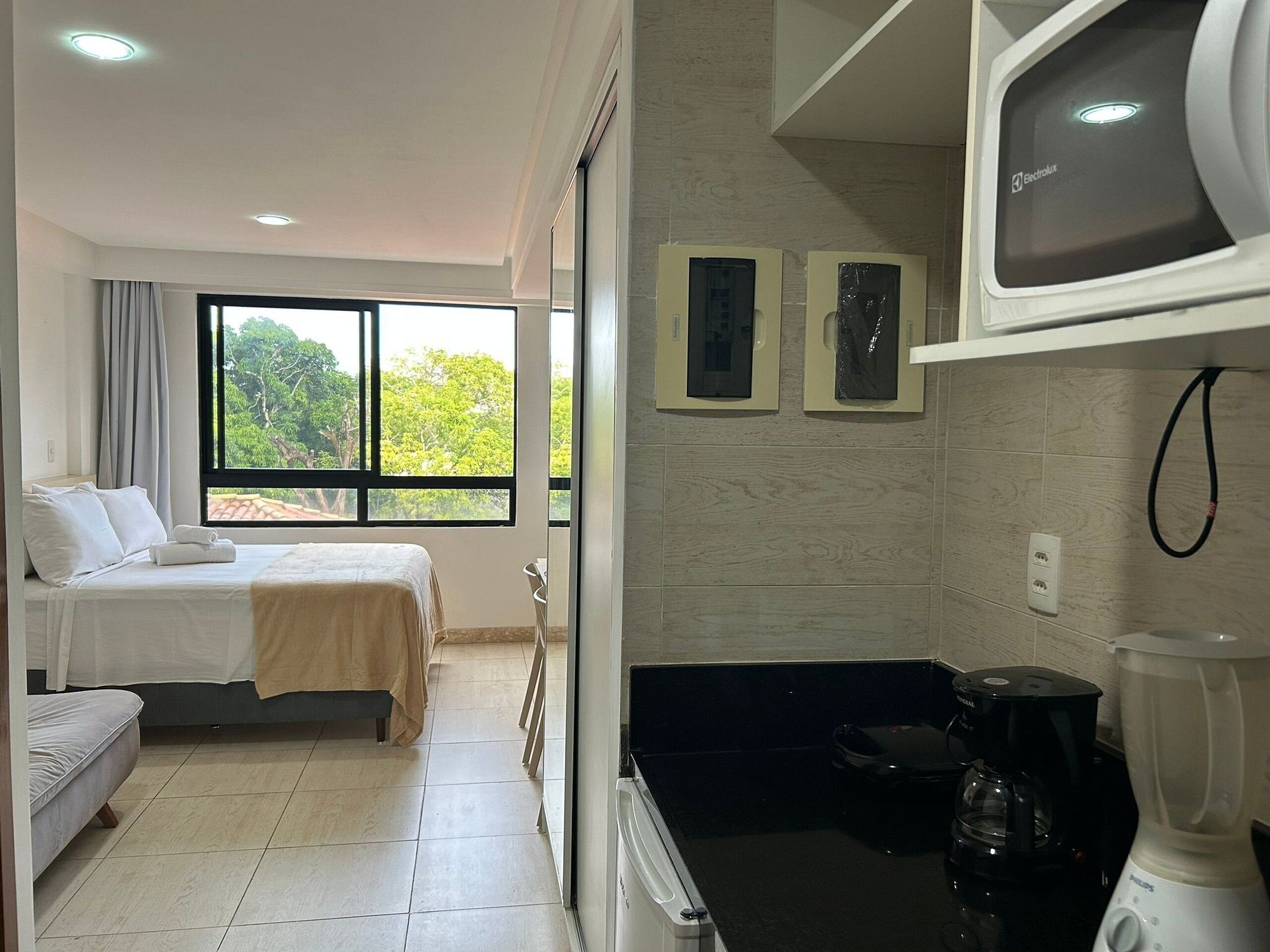 Une chambre d’hôtel avec deux lits, une fenêtre donnant sur la verdure, une kitchenette équipée d’un mixeur et d’un four à micro-ondes.