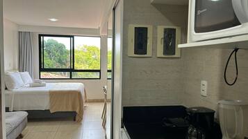 Une chambre d’hôtel avec deux lits, une fenêtre donnant sur la verdure, une kitchenette équipée d’un mixeur et d’un four à micro-ondes.