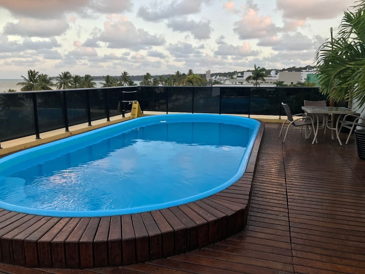 Una piscina con terraza de madera y una mesa con sillas.