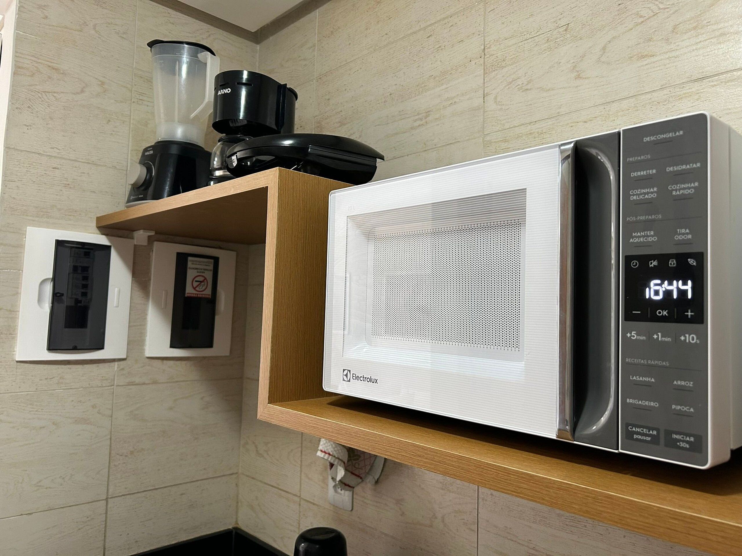 A microwave oven with a digital display, a coffee maker, and a blender on a wooden shelf.