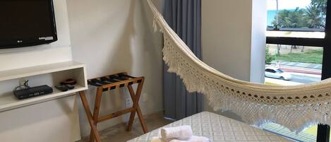 A bedroom with a bed, a TV, a small table, a hammock, and a view of the outdoors.