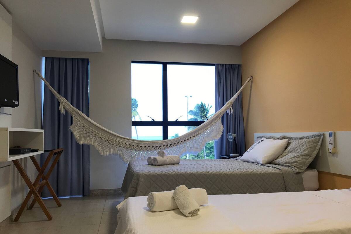 A hotel room with two beds, a TV, a desk, and a hammock.