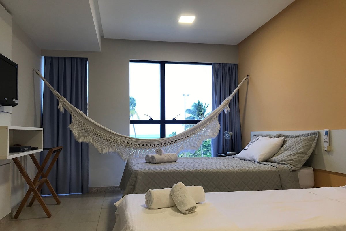 Ein Hotelzimmer mit zwei Betten, einem Fernseher, einem Schreibtisch und einer Hängematte.