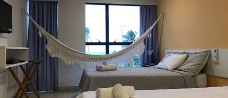 A hotel room with two beds, a TV, a desk, and a hammock.