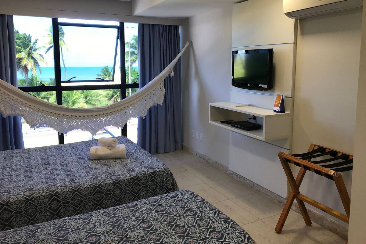 A hotel room with a bed, a hammock, a TV, and a view of the ocean.